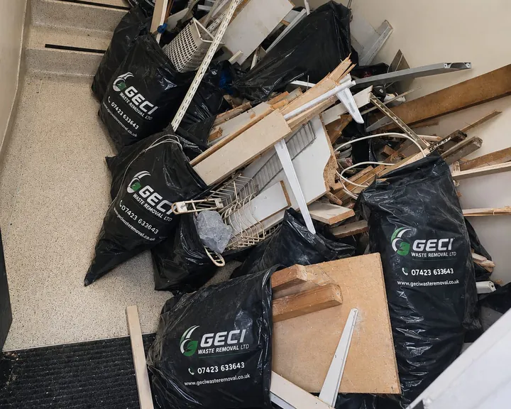 GECI rubbish bags, old shelving, wire baskets and broken timber gathered at the foot of a stairwell, ready to be loaded